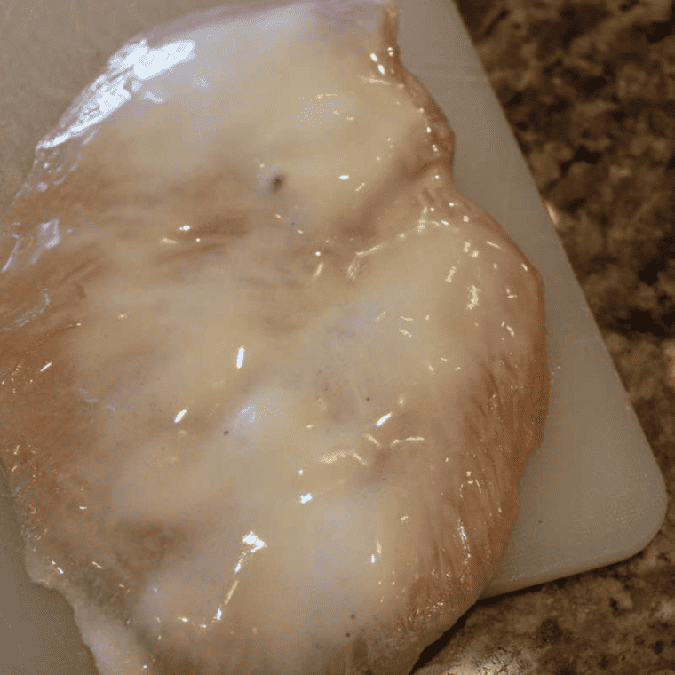Raw chicken breast pounded thin between two sheets of plastic wrap