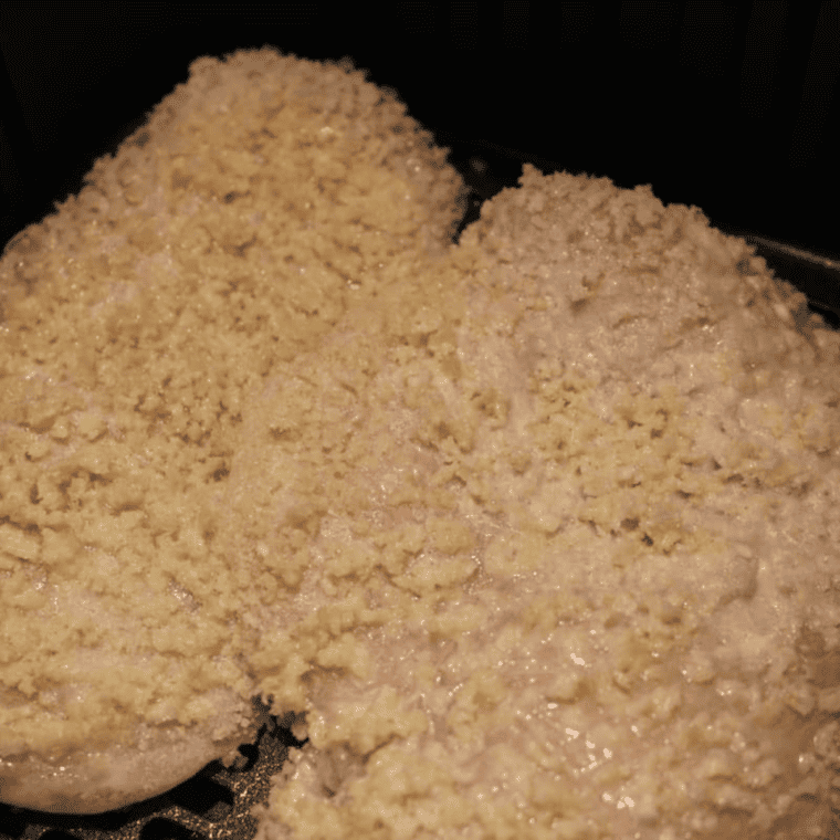 Breaded chicken Milanese cutlets in an air fryer basket before cooking