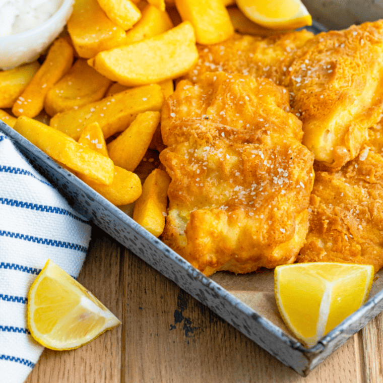 Healthy air-fried fish and chips served with tartar sauce and lemon wedges on a plate.