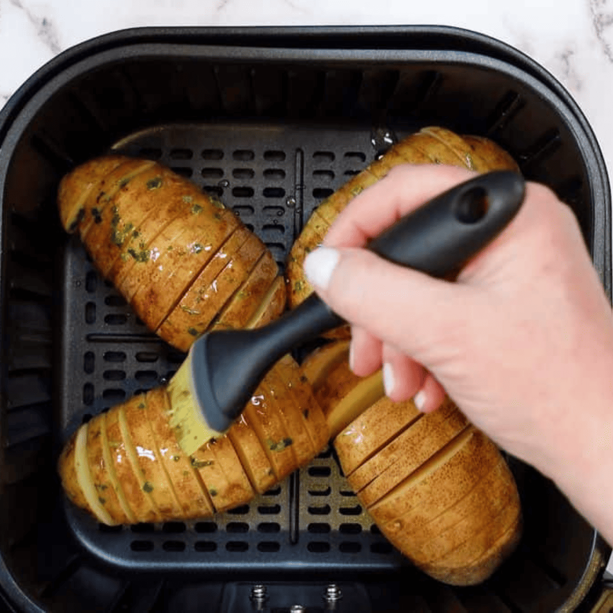 Air fryer basket filled with raw Hasselback potatoes ready to be cooked.