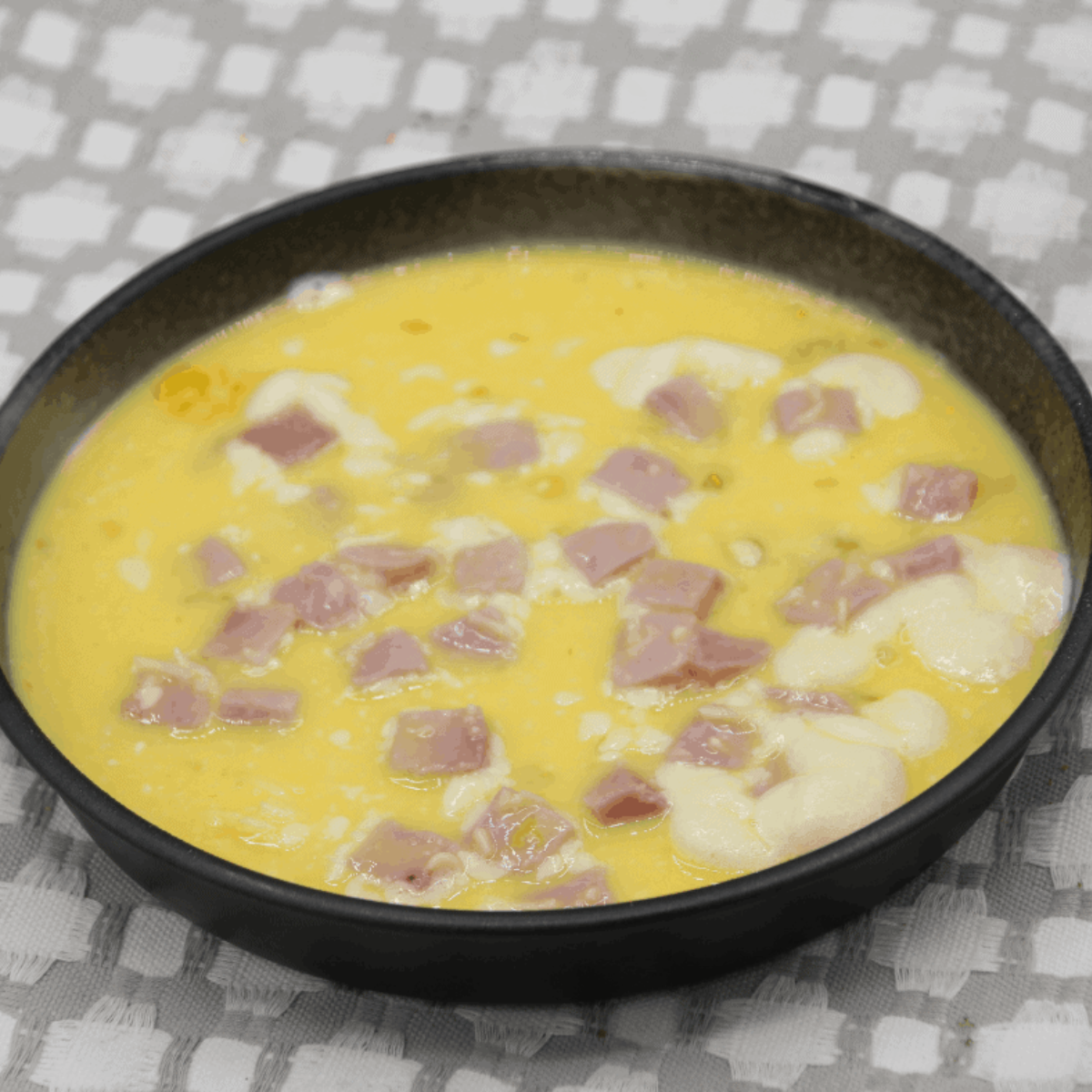 Greased 6-inch round pan filled with whisked egg mixture, topped evenly with diced ham and shredded Swiss cheese, ready to go into the air fryer