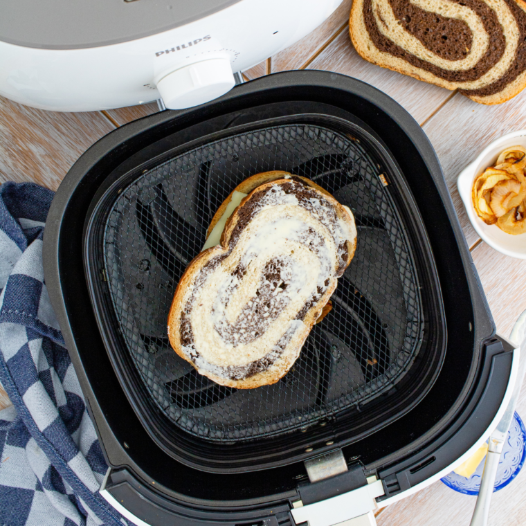 Building an air fryer patty melt with Swiss cheese, beef patty and caramelized onions on buttered rye.