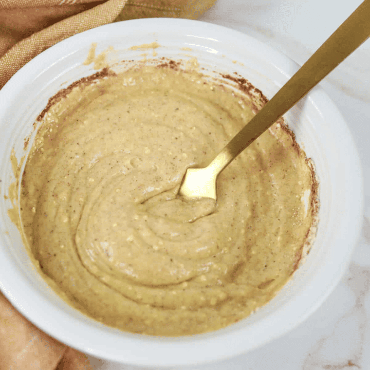 Ramekins brushed with melted butter next to a bowl of cake mix, cinnamon, nutmeg, and milk being mixed together.