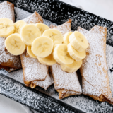 Crispy air fryer peanut butter banana egg rolls dusted with powdered sugar on a white plate