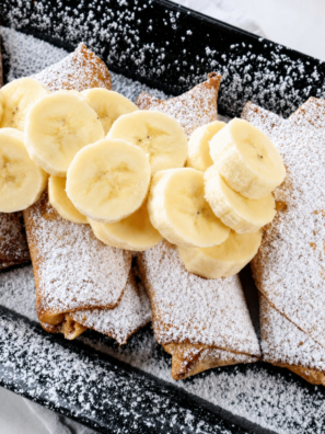 Crispy air fryer peanut butter banana egg rolls dusted with powdered sugar on a white plate