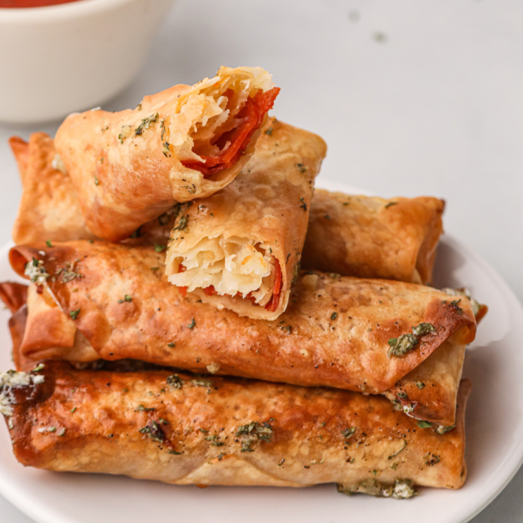 Hand dipping a crispy pizza egg roll into a bowl of warm marinara sauce