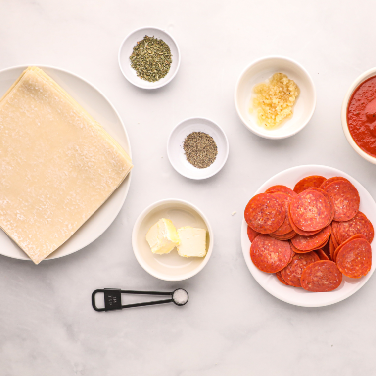 Ingredients for air fryer pizza egg rolls including egg roll wrappers, shredded mozzarella, pepperoni, pizza sauce, and Italian seasoning
