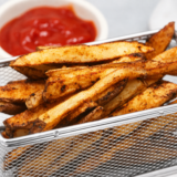 Crispy air fryer spicy french fries in a white bowl with dipping sauce