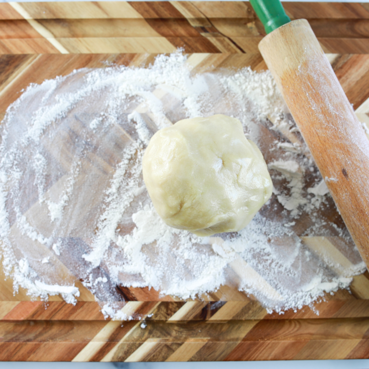 Flouring a flat surface and rolling out cookie dough with a rolling pin.