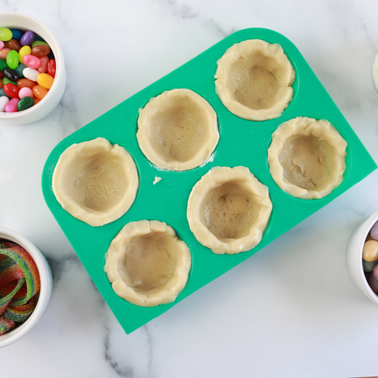 Spraying muffin tin with cooking spray and pressing cookie dough to form basket shapes.