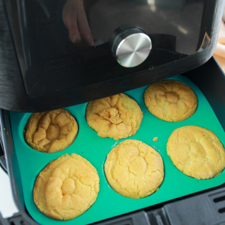 Air fryer muffin pan with cookie dough baking at 300 degrees F and pressing center to form Easter basket hole.