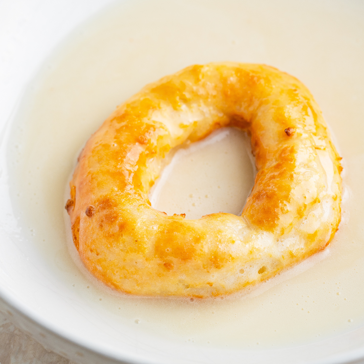 Warm air fryer donut being dipped into shiny vanilla Krispy Kreme-style glaze