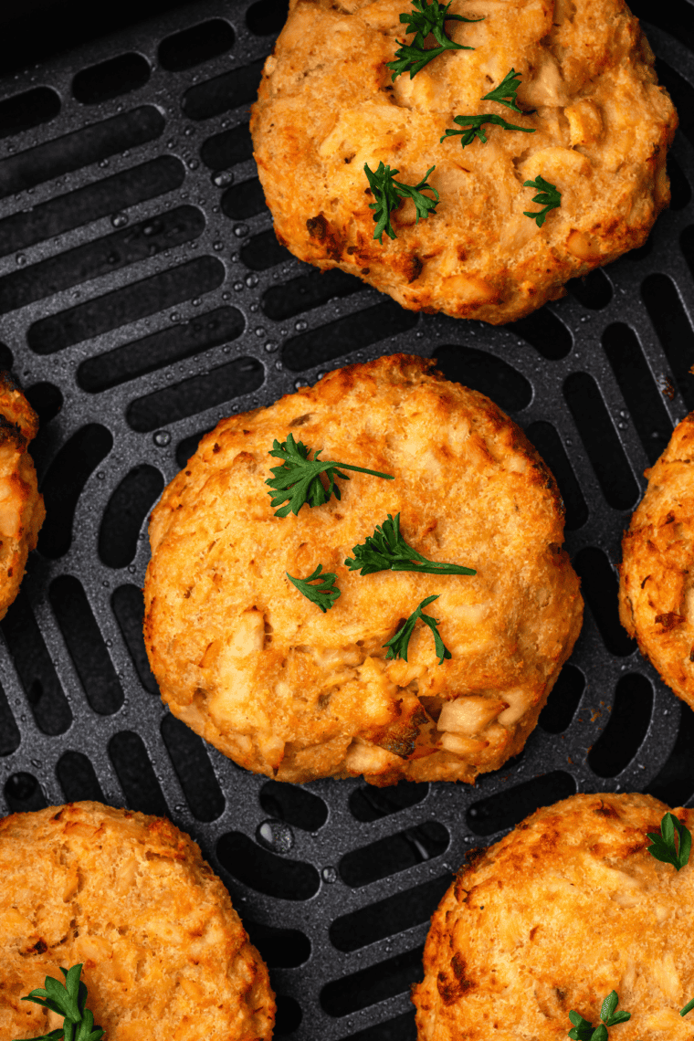 Crispy air fryer salmon patties made with canned salmon, garnished with lemon wedges and fresh herbs on a plate.