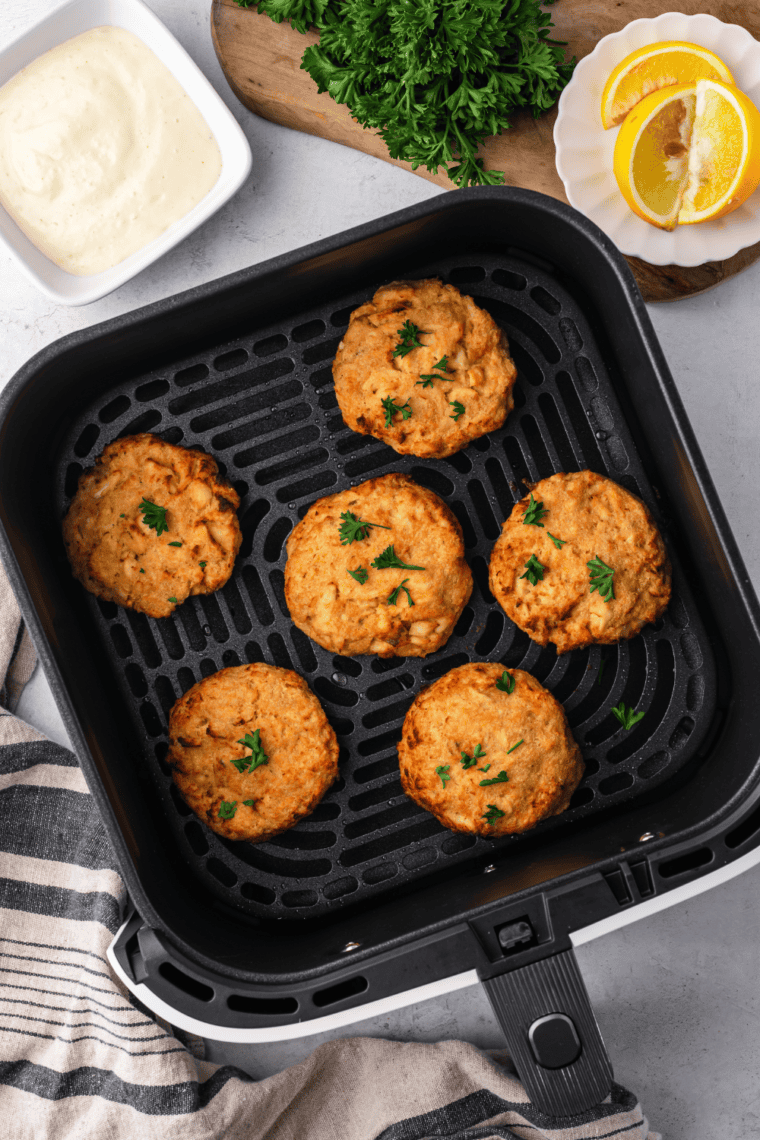 Golden-brown air fryer salmon patties made with canned salmon, served with fresh herbs and lemon wedges.