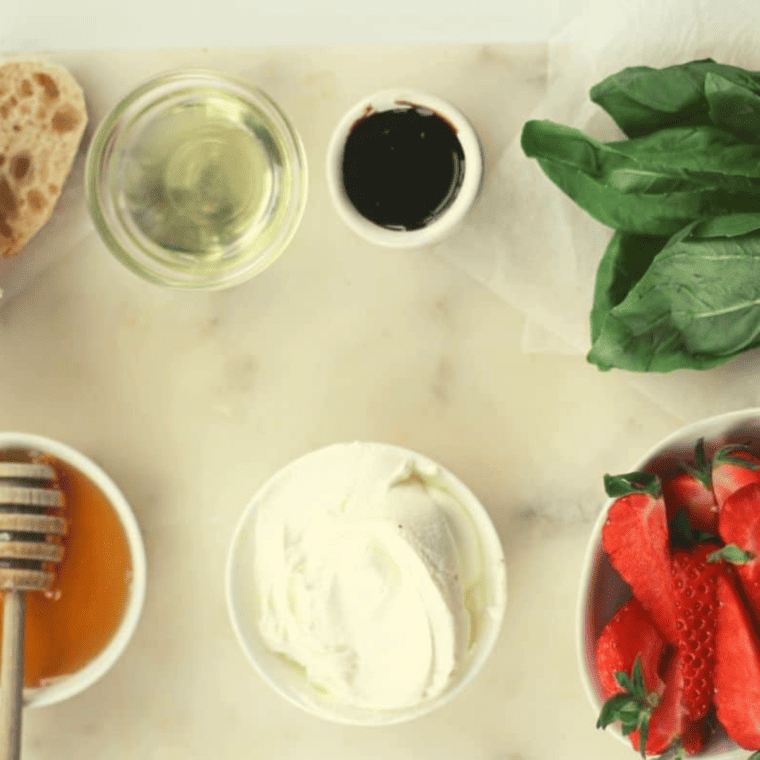 Ingredients for strawberry mascarpone bruschetta: baguette, mascarpone, honey, strawberries, balsamic glaze, and basil