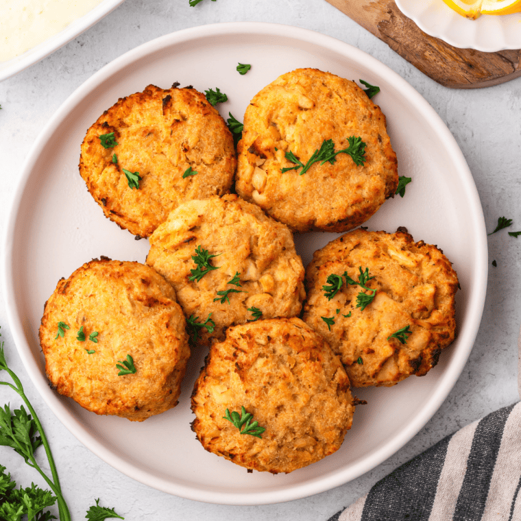 Crispy air fryer salmon patties made with canned salmon, served with lemon wedges and fresh herbs on a white plate.