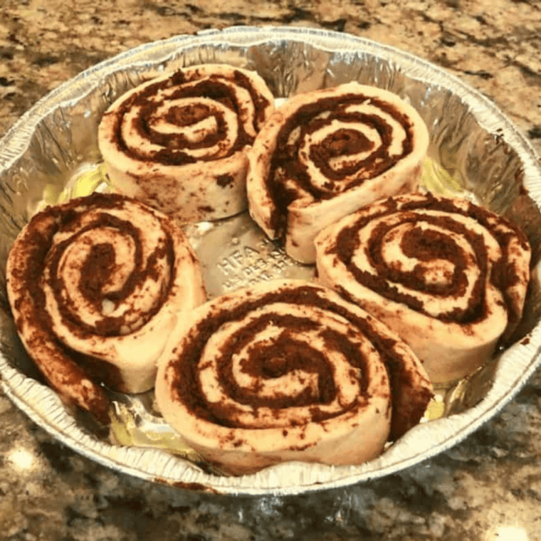 Raw cinnamon rolls placed in a foil pan on a preheated Blackstone griddle