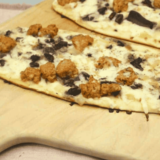 Blackstone griddle cooking a sausage and mushroom flatbread pizza with crispy crust and melted cheese.