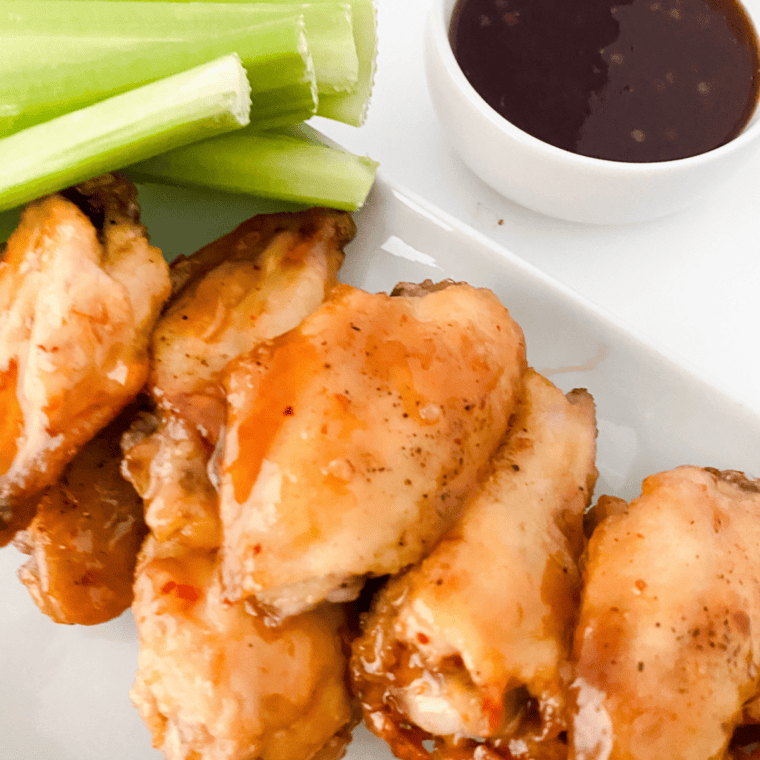 Plate of crispy chicken wings coated in sweet and tangy Hawaiian-style sauce, served hot and garnished.