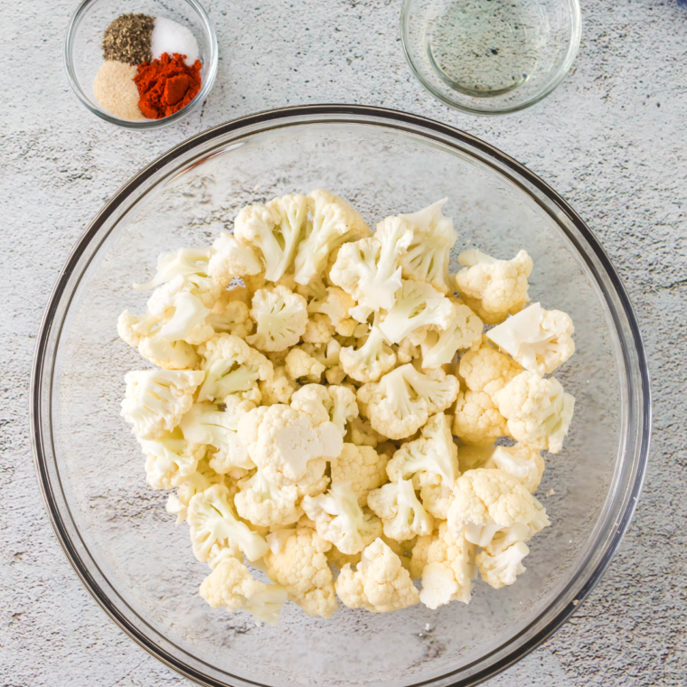 Frozen cauliflower tossed in buffalo sauce and olive oil in bowl.