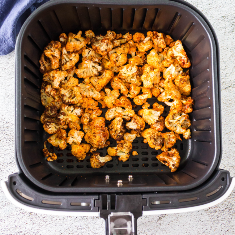 Coated cauliflower florets arranged in air fryer basket, ready to cook.