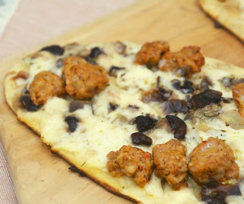 Blackstone griddle cooking sausage and mushroom flatbread pizza with melted cheese and golden crust.