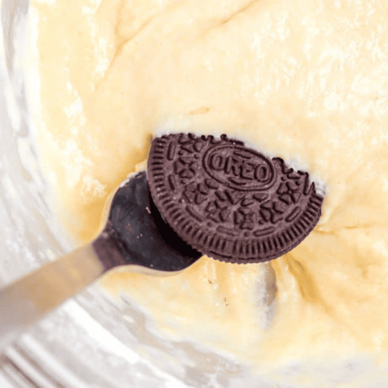 Oreos being dipped in pancake batter with a fork, excess batter dripping, placed on parchment-lined air fryer tray.