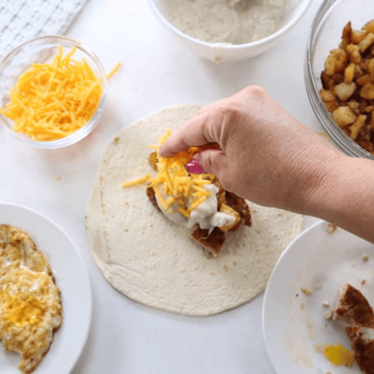 A tortilla topped with diced fried eggs and a generous sprinkle of shredded cheddar cheese, ready to be wrapped.