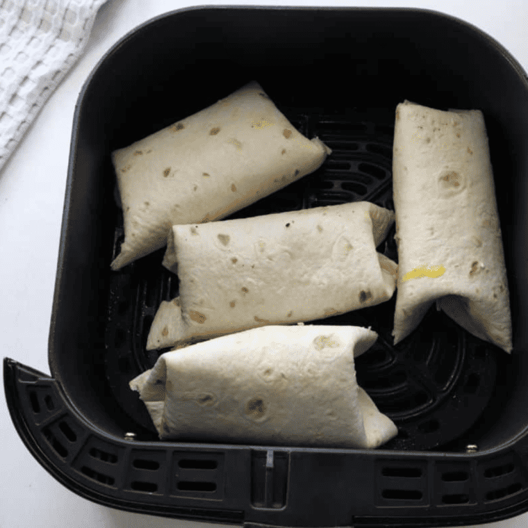 A wrapped burrito placed in an air fryer basket, ready to cook at 390°F for 2-3 minutes until crispy and golden.