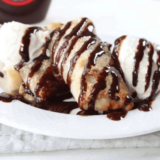 Air fryer cookie dough egg rolls stacked on a white plate, one cut open showing melted chocolate chips inside