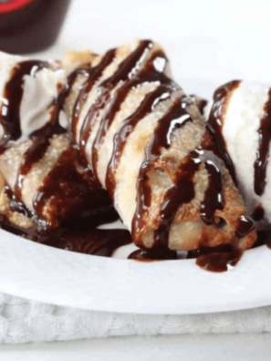 Air fryer cookie dough egg rolls stacked on a white plate, one cut open showing melted chocolate chips inside