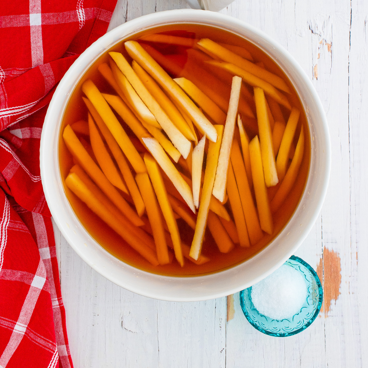 Peeled Russet potatoes sliced into thin strips soaking in iced water for crispy French fries