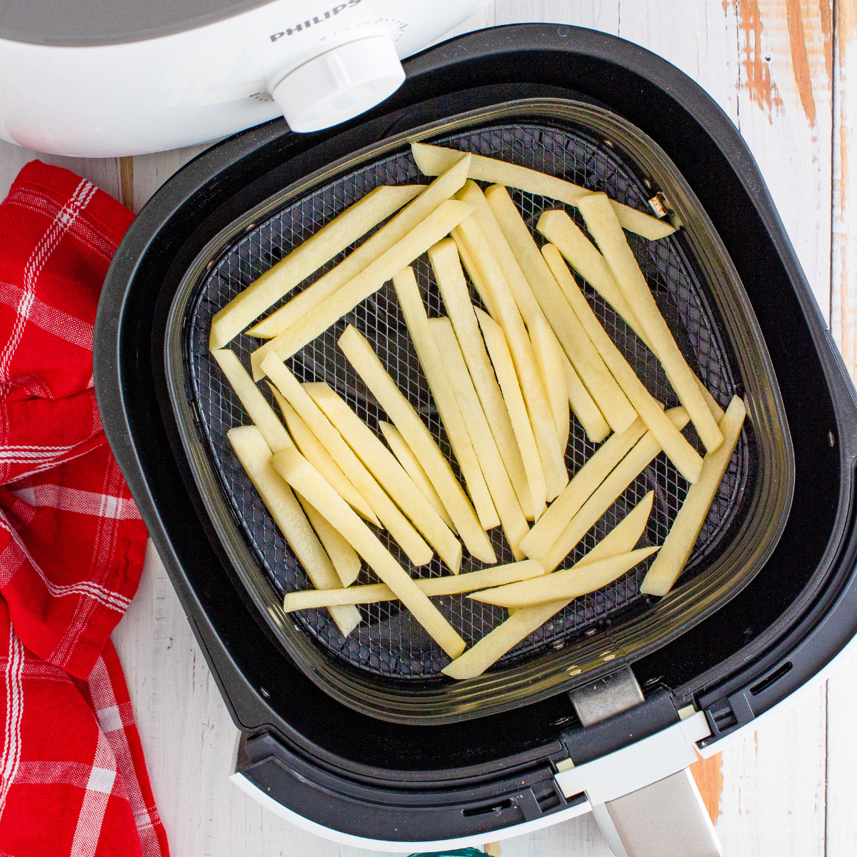 Raw potato strips tossed with olive oil, arranged in air fryer basket, cooking until golden brown and seasoned with sea salt