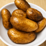 Crispy air fryer fingerling potatoes on a white plate with blistered skins and flecks of kosher salt