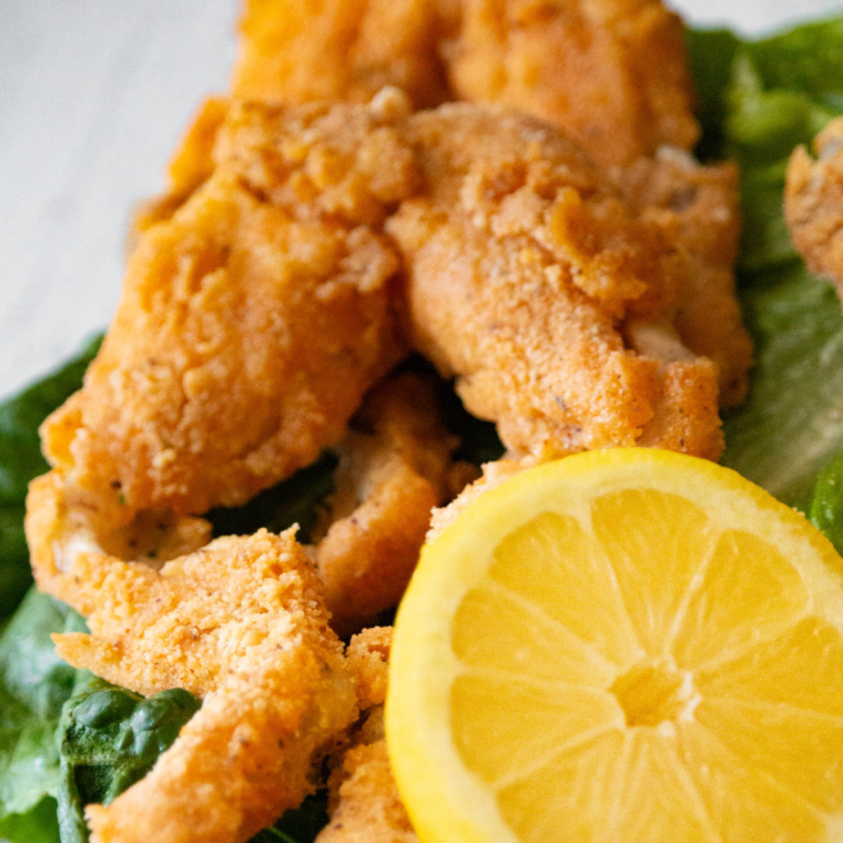 Golden, crispy air fryer frog legs served on a plate, garnished with fresh herbs.