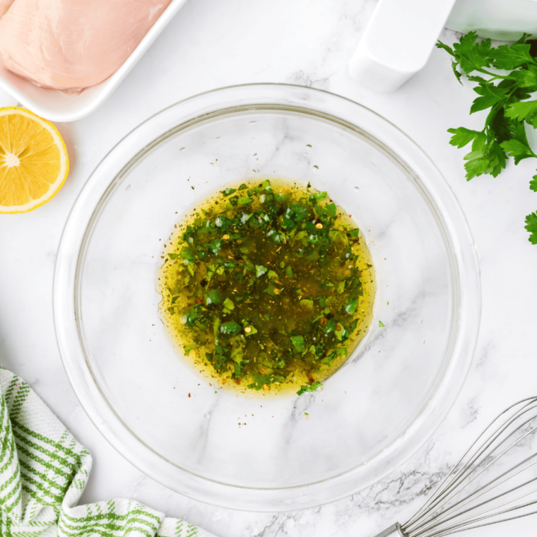 Marinated chicken breasts soaking in Italian dressing in a glass bowl.