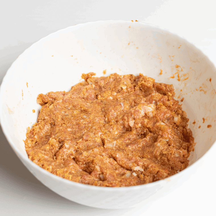 Mixing ground meats, breadcrumbs, cheese, sautéed vegetables, eggs, and marinara in a large bowl.
