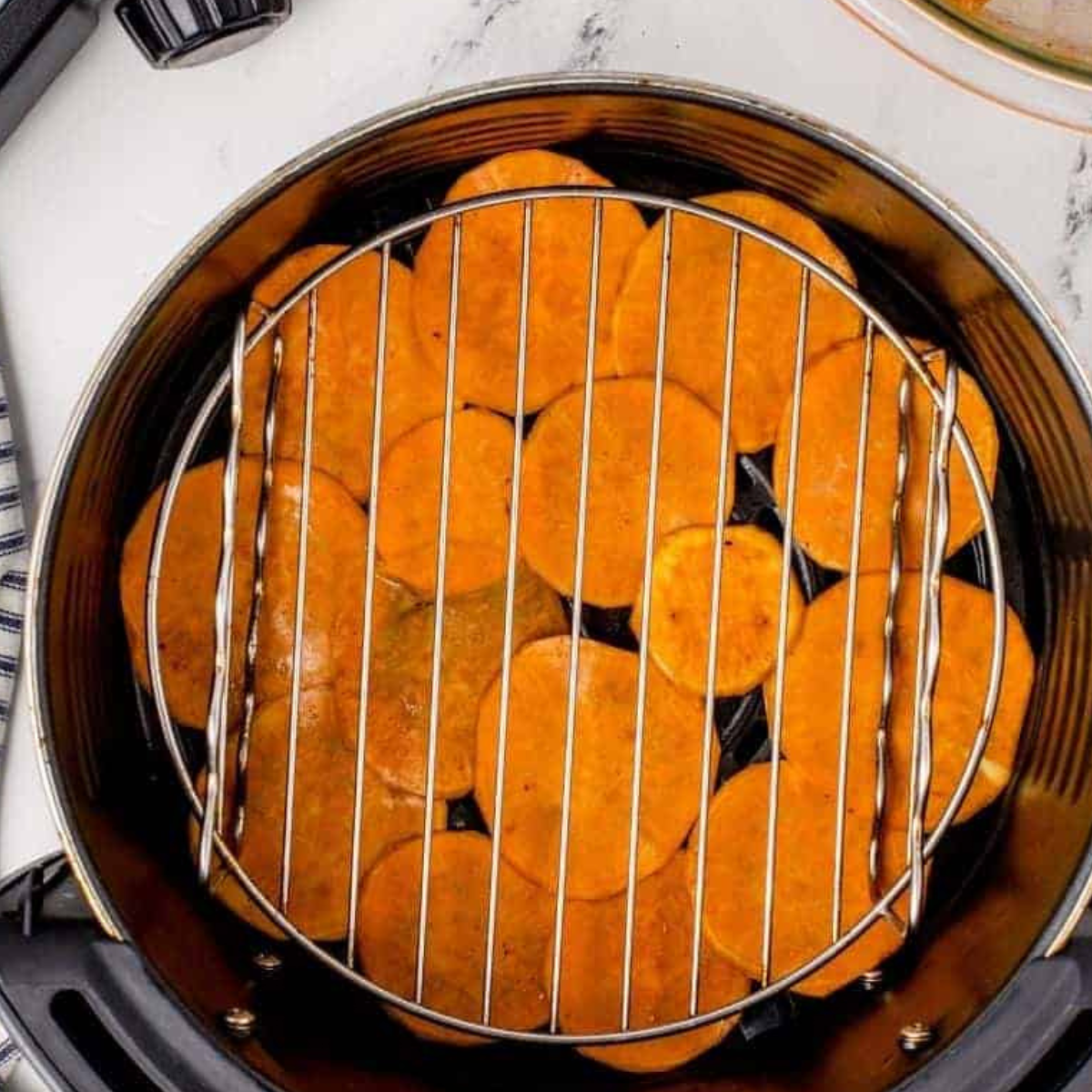 Arranging sweet potato slices in the air fryer basket in a single layer.