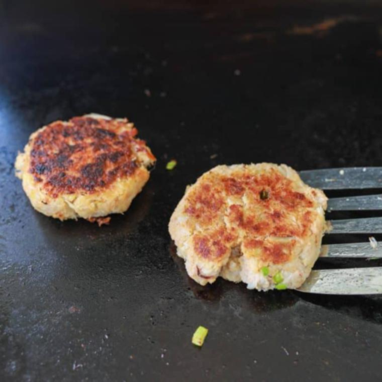 Golden crab cakes being flipped with a spatula on the Blackstone flat top griddle