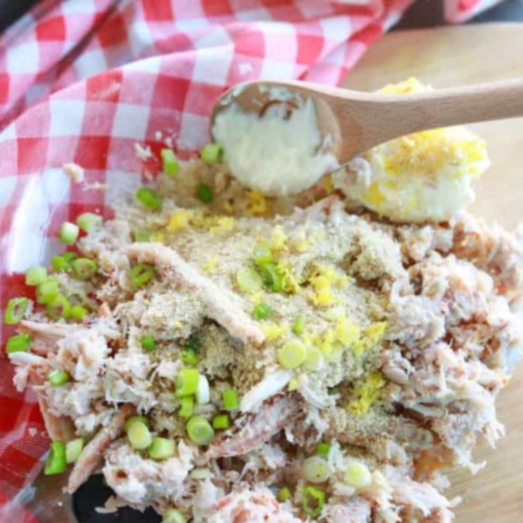 Lump crab meat and seasonings being gently folded together in a glass mixing bowl