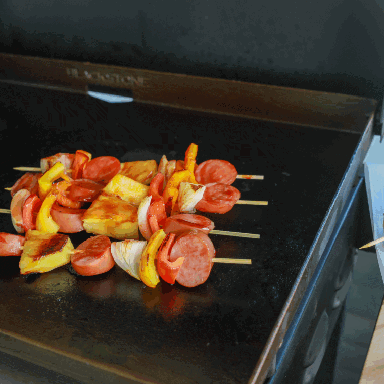 Hawaiian kielbasa kabobs with pineapple and bell peppers cooking on a Blackstone griddle.