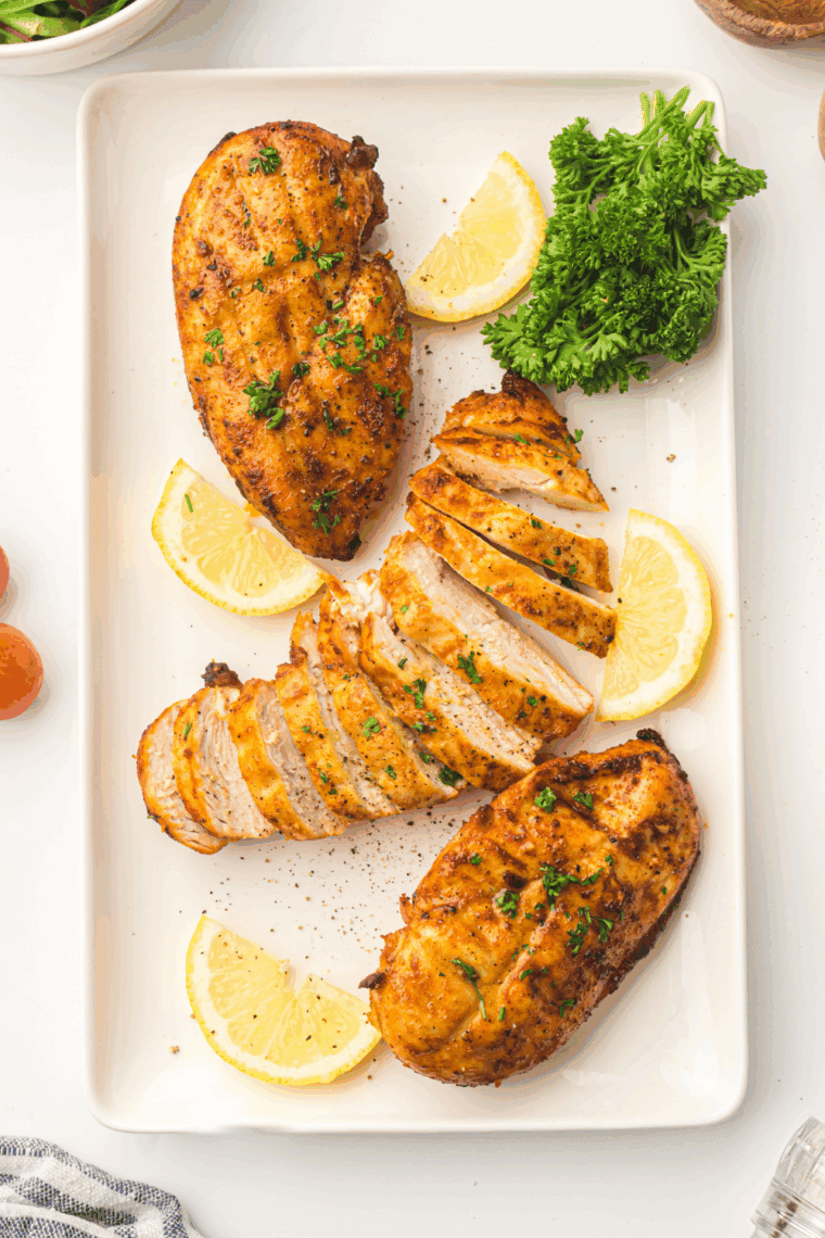Air Fryer Lemon Garlic Chicken Breast cooked golden brown, juicy inside, garnished with fresh lemon slices and herbs.