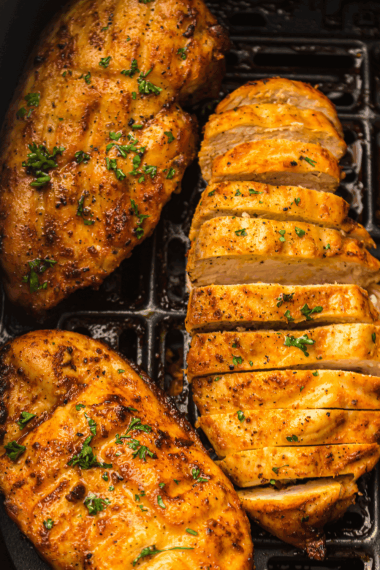 Boneless lemon garlic chicken breasts cooking in a greased air fryer basket, ready to turn golden brown and juicy.