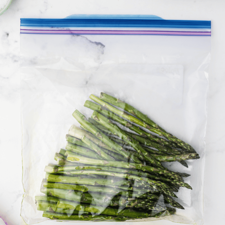 Asparagus being tossed with olive oil and salt in a bowl for even coating.