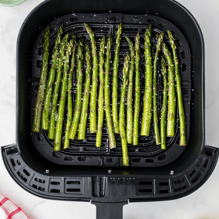 Asparagus arranged in a single layer in the air fryer basket, ready to cook at 400°F for 6-8 minutes.