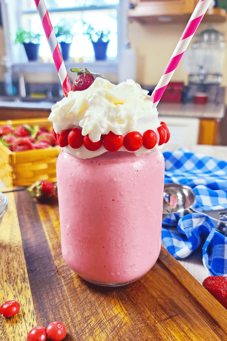 Pink Skittles Strawberry Milkshake in a glass topped with whipped cream and rainbow Skittles candy pieces.