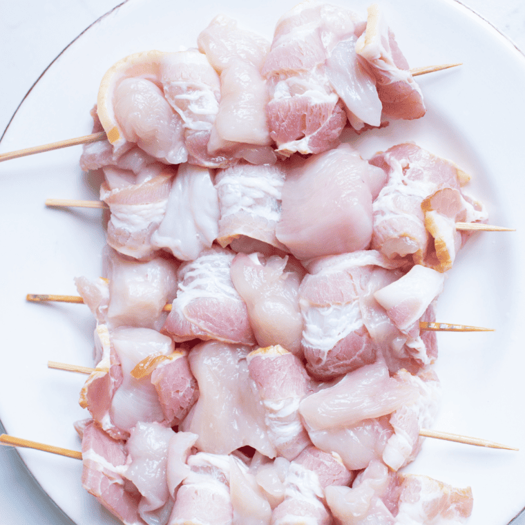 Wrap a piece of chicken with bacon and secure with a toothpick, repeating for all pieces.