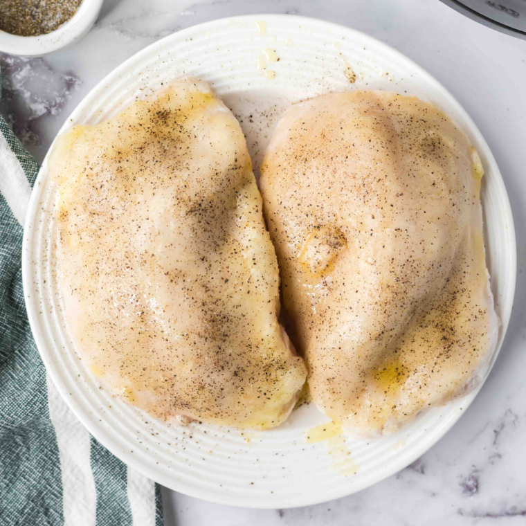 Air Fryer Frozen Chicken Breasts being seasoned with salt, pepper and brushed with olive oil.