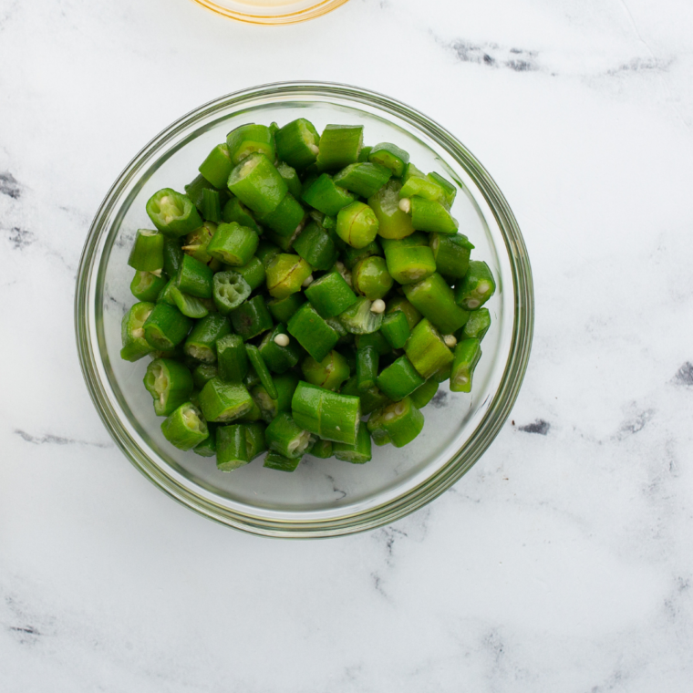 Frozen okra tossed with oil and seasonings in a mixing bowl