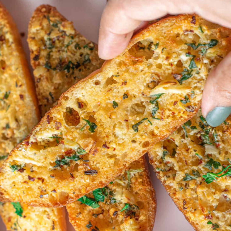Close-up stack of homemade air fryer garlic bread with fresh herbs.